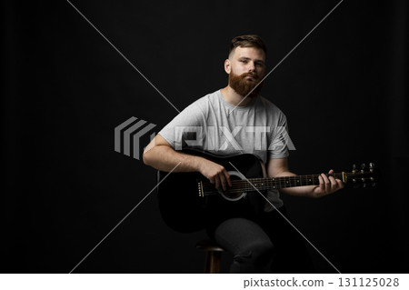 Bearded man in grey t-shirt playing acoustic guitar on dark background Bearded man in grey t-shirt playing acoustic guitar on dark background 131125028