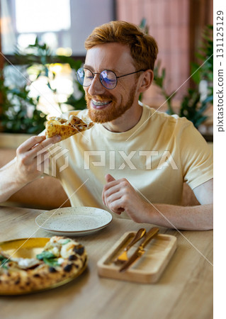 Ginger man smiling while enjoying pizza in bright dining place 131125129