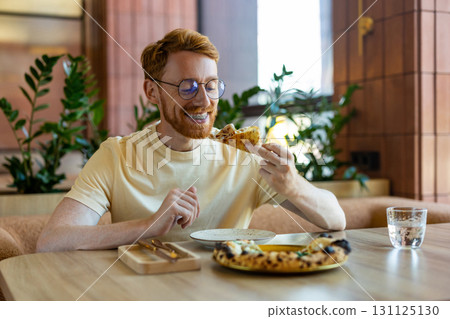 Bearded man in yellow shirt sitting at cafe table with pizza Bearded man in yellow shirt sitting at cafe table with pizza 131125130