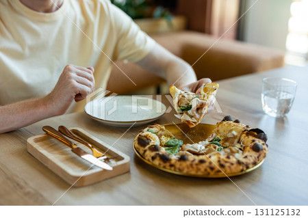 Unrecognizable man in casual outfit eating fresh pizza at wooden table Unrecognizable man in casual outfit eating fresh pizza at wooden table 131125132