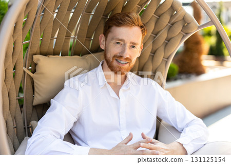 Red-haired man in white shirt posing in outdoor lounge chair Red-haired man in white shirt posing in outdoor lounge chair 131125154