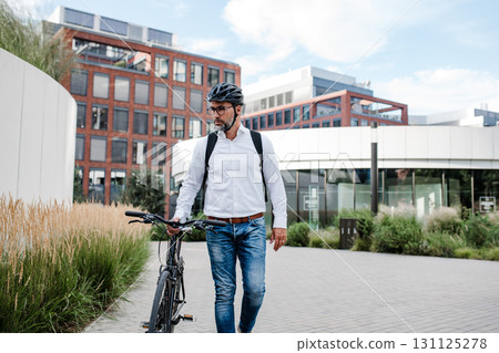 City commuter walking with bike to office, wearing backpack and helmet. 131125278