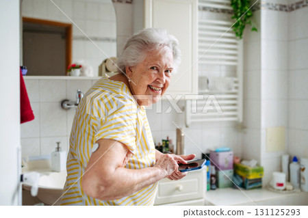 Older woman in bathroom, with smartphone. Older woman in bathroom, with smartphone. 131125293