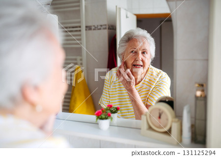 Older woman checking skin and appearance in bathroom. Older woman checking skin and appearance in bathroom. 131125294
