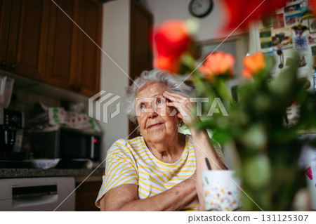 Portrait of worried senior woman sitting in kitchen. Portrait of worried senior woman sitting in kitchen. 131125307