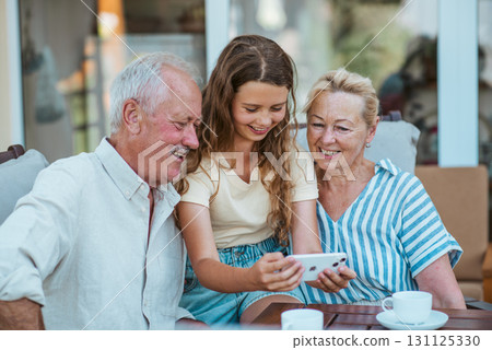 Granddaughter looking at photos in smartphone with older grandparents. 131125330