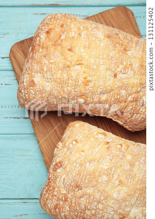 Ciabatta rustic bread on cutting board on blue background. Vertical photo Ciabatta rustic bread on cutting board on blue background. Vertical photo 131125402