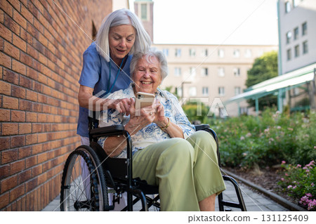 Senior patient in wheelchair showing picture in smartphone to caregiver. 131125409