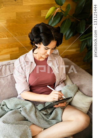 Woman with hair rollers journaling in the morning, using tablet. Woman with hair rollers journaling in the morning, using tablet. 131125444