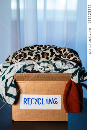 Cardboard box full of clothes labeled Recycling. Concept of sustainable fashion and responsible wardrobe management. 131125551