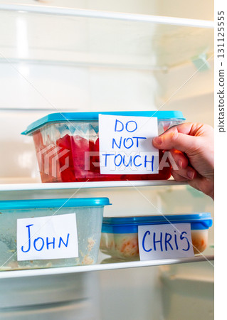Do Not Touch sticker on lunch boxes in office refrigerator. Angry and hungry workers concept. 131125555