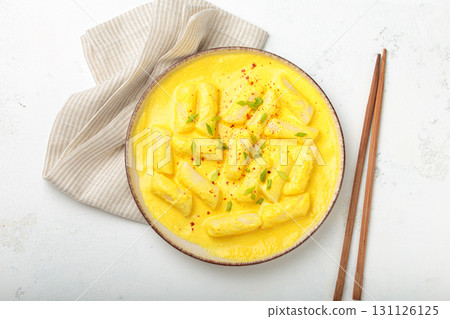 Traditional korean tteokbokki in creamy cheese sauce with garnish, wooden chopsticks on rustic white background top view Traditional korean tteokbokki in creamy cheese sauce with garnish, wooden chopsticks on rustic white background top view 131126125