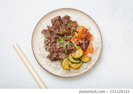 Korean beef bulgogi bowl dish with rice, roasted meat, kimchi and marinated cucumber on white background top view with chopsticks Korean beef bulgogi bowl dish with rice, roasted meat, kimchi and marinated cucumber on white background top view with chopsticks 131126131