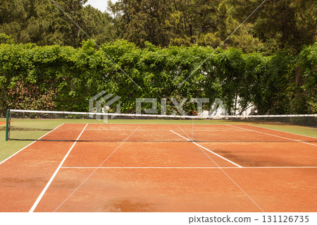 Empty tennis clay court surrounded by green hedge in a sunny day 131126735