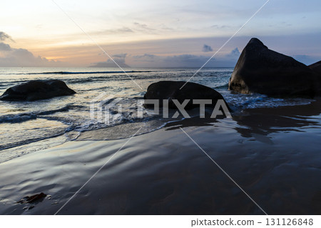 Beach landscape with wet sand, shore water and dark silhouettes of coastal rocks Beach landscape with wet sand, shore water and dark silhouettes of coastal rocks 131126848