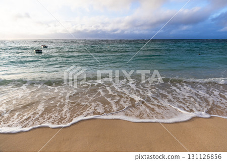 A tranquil coastal view featuring soft waves washing onto sandy shore 131126856