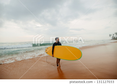 Young handsome male surfer with a surfboard on a sandy beach at ocean . Summer, vacation, sea Young handsome male surfer with a surfboard on a sandy beach at ocean . Summer, vacation, sea 131127033