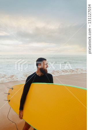 Young bearded man with surfboard standing near a beach. Man with surfing board outdoors on a summer day. Young bearded man with surfboard standing near a beach. Man with surfing board outdoors on a summer day. 131127034