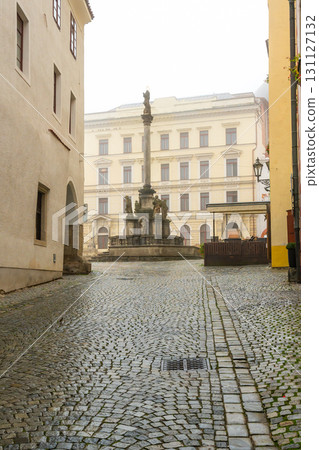 A moody autumn view of the square in Cesky Krumlov, featuring the Baroque Plague Column with the statue of Virgin Mary Immaculata, surrounded by mist, rain, and a tranquil atmosphere 131127132