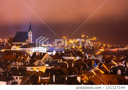 A panoramic night view of Cesky Krumlov, showcasing the rooftops, illuminated buildings, and the Church of St. Vitus beautifully lit up against the dark sky 131127144