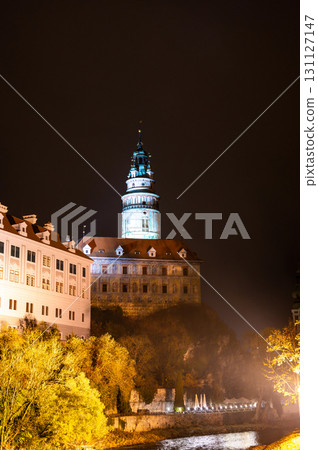 A stunning night view of the illuminated tower of Cesky Krumlov Castle towering above the Vltava River, creating a magical atmosphere with the reflection in the water A stunning night view of the illuminated tower of Cesky Krumlov Castle towering above the Vltava River, creating a magical atmosphere with the reflection in the water 131127147