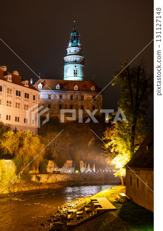 A stunning night view of the illuminated tower of Cesky Krumlov Castle towering above the Vltava River, creating a magical atmosphere with the reflection in the water A stunning night view of the illuminated tower of Cesky Krumlov Castle towering above the Vltava River, creating a magical atmosphere with the reflection in the water 131127148