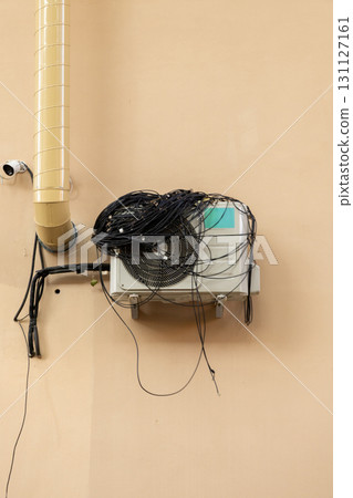 An air conditioner with large coil of wires for connection is installed on facade of the house.  131127161