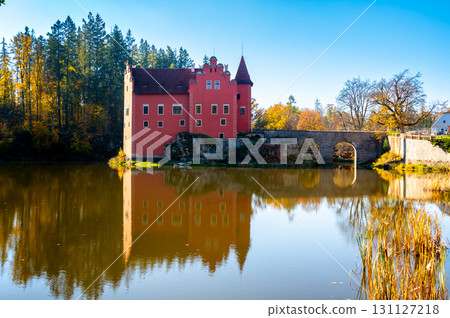 Panoramic view of Cervena Lhota Castle in the Czech Republic, surrounded by a lake reflecting its image. Autumn trees in vibrant colors and sunny weather create a picturesque, serene scene. 131127218