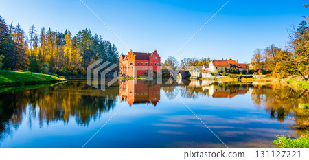 Panoramic view of Cervena Lhota Castle in the Czech Republic, surrounded by a lake reflecting its image. Autumn trees in vibrant colors and sunny weather create a picturesque, serene scene. Panoramic view of Cervena Lhota Castle in the Czech Republic, surrounded by a lake reflecting its image. Autumn trees in vibrant colors and sunny weather create a picturesque, serene scene. 131127221