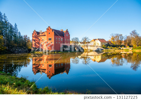 Panoramic view of Cervena Lhota Castle in the Czech Republic, surrounded by a lake reflecting its image. Autumn trees in vibrant colors and sunny weather create a picturesque, serene scene. Panoramic view of Cervena Lhota Castle in the Czech Republic, surrounded by a lake reflecting its image. Autumn trees in vibrant colors and sunny weather create a picturesque, serene scene. 131127225