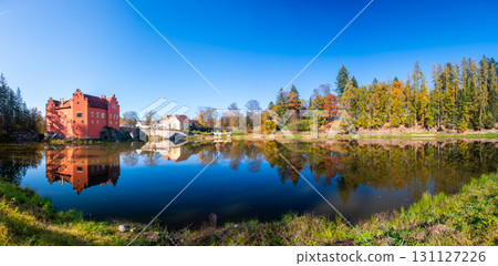 Panoramic view of Cervena Lhota Castle in the Czech Republic, surrounded by a lake reflecting its image. Autumn trees in vibrant colors and sunny weather create a picturesque, serene scene. Panoramic view of Cervena Lhota Castle in the Czech Republic, surrounded by a lake reflecting its image. Autumn trees in vibrant colors and sunny weather create a picturesque, serene scene. 131127226