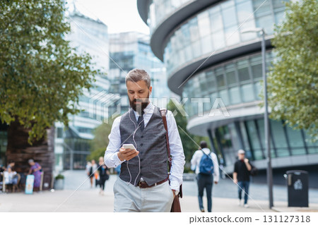 Handsome businessman in front of buildings in business district, looking at phone. 131127318