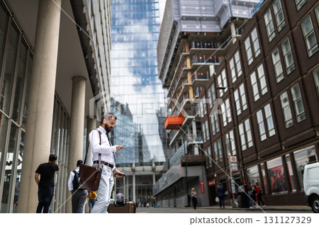 Man with suitcase walking down the street, looking at phone. 131127329