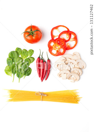 A flat lay of spaghetti and various fresh vegetables, including a tomato, bell pepper slices, spinach, chili peppers, and mushrooms, on a white background 131127462