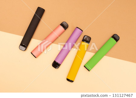 An overhead shot of five colorful disposable vapes on a beige background. An overhead shot of five colorful disposable vapes on a beige background. 131127467
