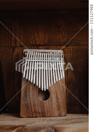 A wooden kalimba (thumb piano) stands on a dark, textured wooden background, illuminated by dramatic studio lighting. 131127468