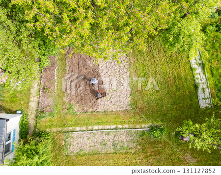 Young farmer man is cultivating the field with machine. Aerial drone top down view of small field in old fashioned garden. Concept of home agriculture. 131127852