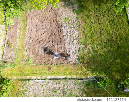 Young farmer man is cultivating the field with machine. Aerial drone top down view of small field in old fashioned garden. Concept of home agriculture. 131127854
