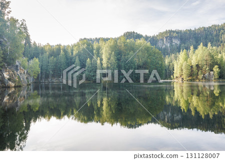 The Piskovna lake in Adrspach-Teplice Rocks area, in Hradec Kralove Region in the Czech Republic, Europe. Reflections of towering trees dance on a tranquil lake, mirroring the sky's gentle embrace. 131128007