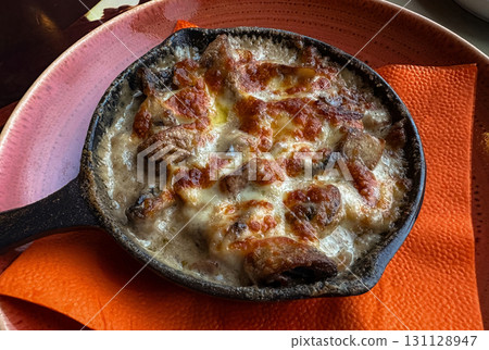 An appetizing high-angle shot of a bubbling, cheesy dish served in a small cast-iron skillet. An appetizing high-angle shot of a bubbling, cheesy dish served in a small cast-iron skillet. 131128947