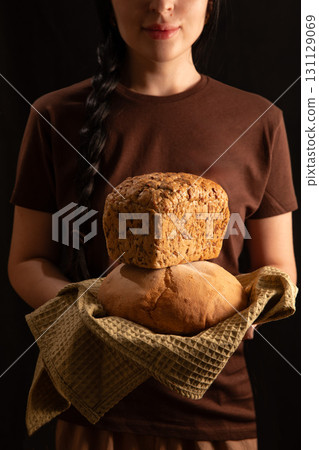 brunette girl in a brown T shirt holds a loaf of bread in her hands displaying it with care. The warm atmosphere suggests a homey baking experience in the kitchen. brunette girl in a brown T shirt holds a loaf of bread in her hands displaying it with care. The warm atmosphere suggests a homey baking experience in the kitchen. 131129069