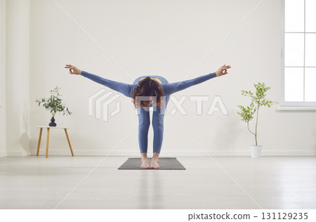 Attractive yogi woman working out, beautiful model doing yoga exercise on mat, standing Attractive yogi woman working out, beautiful model doing yoga exercise on mat, standing 131129235