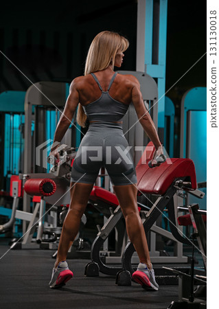 blonde woman is at the gym performing exercises with dumbbells. She showcases her strong physique and determination as she works out in a vibrant fitness environment. blonde woman is at the gym performing exercises with dumbbells. She showcases her strong physique and determination as she works out in a vibrant fitness environment. 131130018