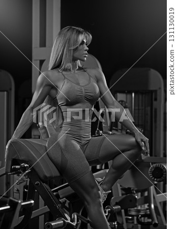 blonde woman is engaged in strength training at a gym during evening hours. She is using gym equipment to enhance her fitness showcasing her dedication to health. 131130019