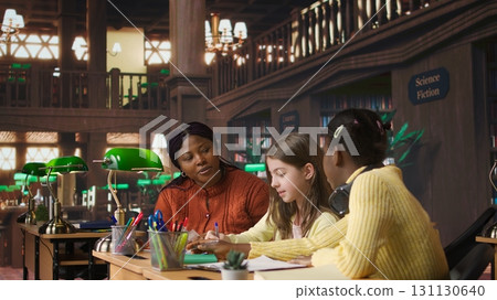 Black teacher mentoring her teen girls students with an assignment, teaching academic concepts and enhancing their knowledge through practical exercises. Private lessons at the library. Camera A. Black teacher mentoring her teen girls students with an assignment, teaching academic concepts and enhancing their knowledge through practical exercises. Private lessons at the library. Camera A. 131130640