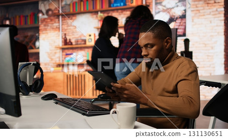 Startup entrepreneur in wheelchair using tablet to do research, looking to grow value of company. Venture business manager with disability using device, developing innovative growth strategy, camera A 131130651