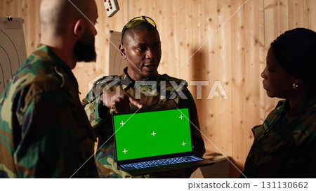 Team of military units at shooting range watching video on isolated screen laptop to learn necessary combat skills. Army soldiers looking at instructions on mockup notebook during training, camera A Team of military units at shooting range watching video on isolated screen laptop to learn necessary combat skills. Army soldiers looking at instructions on mockup notebook during training, camera A 131130662