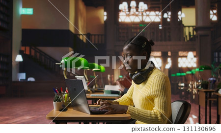 Teenager girl working on a foreign language assignment in the school library, consulting books and dictionaries to finish the homework project. Productive study habits and research at desk. Camera A. 131130696