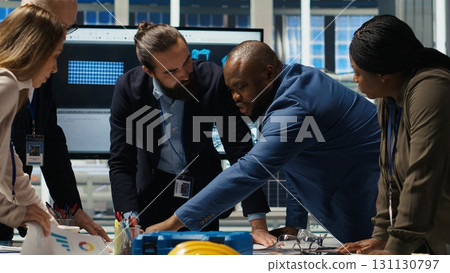 Factory management looking over schematics, working together to expand production. Industrial plant executives doing brainstorming, discussing over blueprint of facility layout, camera B Factory management looking over schematics, working together to expand production. Industrial plant executives doing brainstorming, discussing over blueprint of facility layout, camera B 131130797