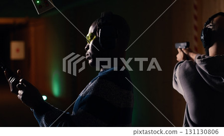 Shooting range customer ending shooting targets session after learning to operate handgun in close quarters. Man leaving indoor shooting ground after finishing firing lethal fire weapon, camera B Shooting range customer ending shooting targets session after learning to operate handgun in close quarters. Man leaving indoor shooting ground after finishing firing lethal fire weapon, camera B 131130806